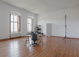 A desk with electronics equipment and a satellite communication antenna seen inside a large, lofty studio with white walls 