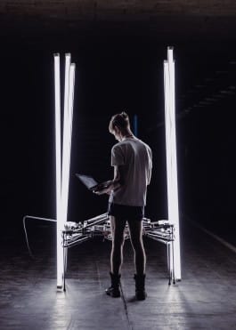 media artis michael candy in front of his artwork cryptid, a 6-legged robot walking on led-bars 